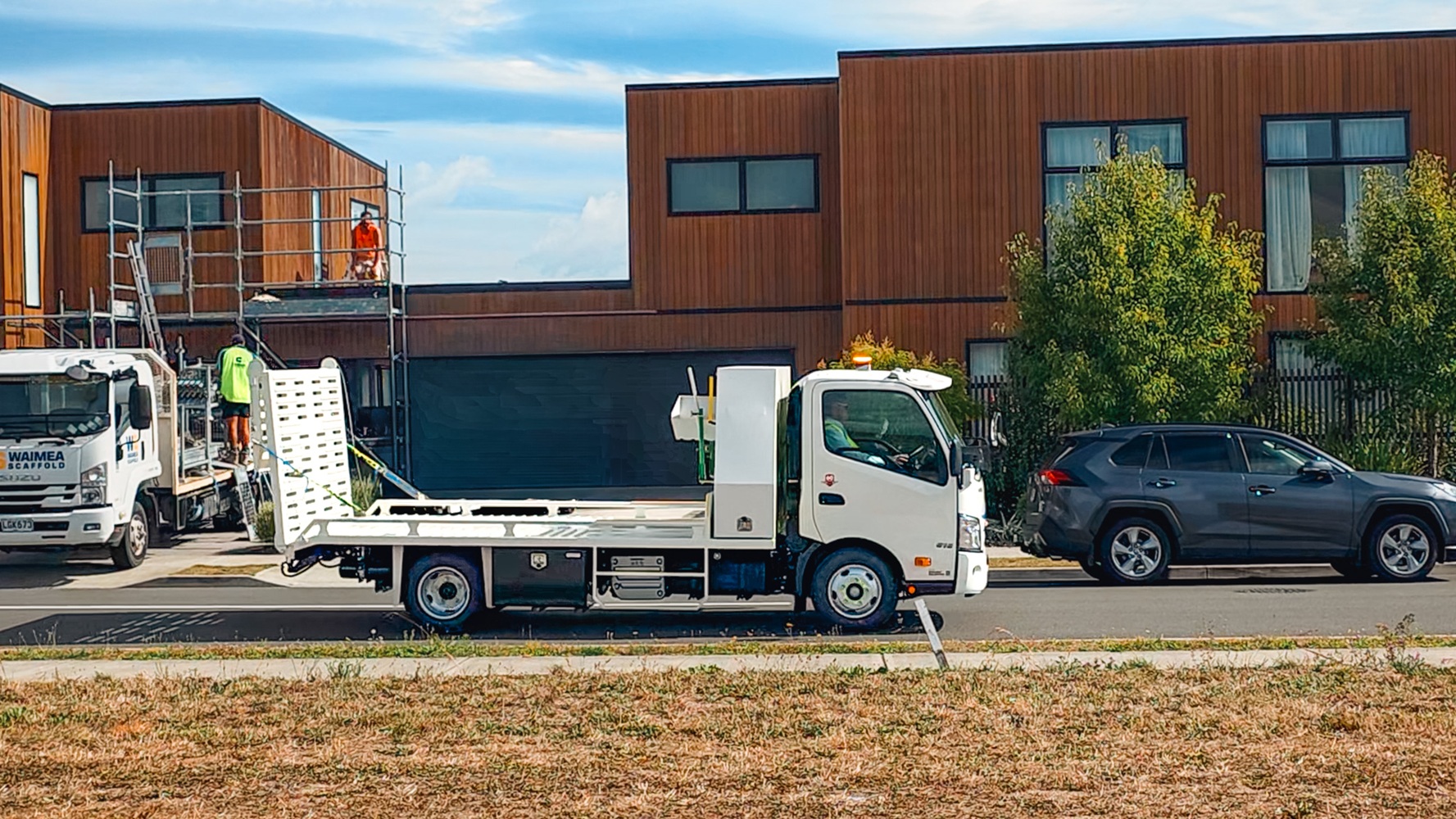 A compact Class 1 transporter truck with a split hydraulic ramp on the back and toolboxes mounted behind the cab.