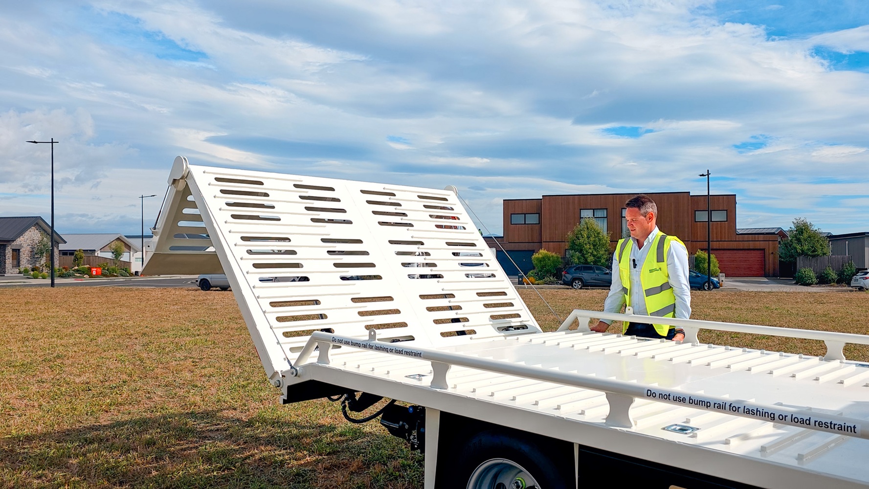 A compact Class 1 transporter truck with a split hydraulic ramp on the back and toolboxes mounted behind the cab.