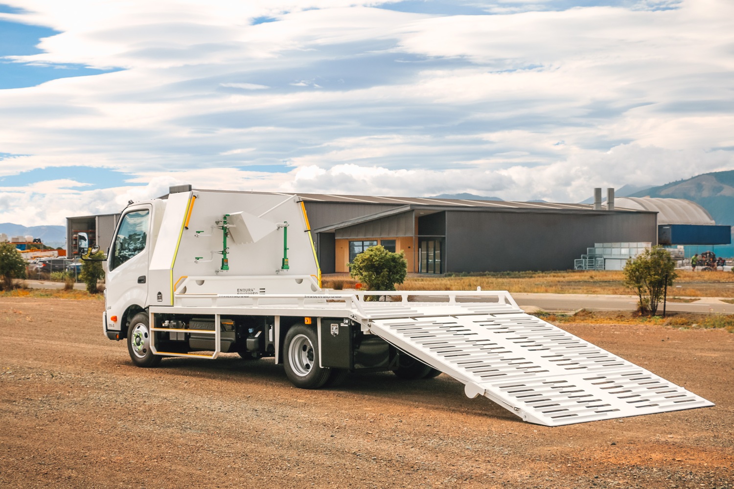 A compact Class 1 transporter truck with a split hydraulic ramp on the back and toolboxes mounted behind the cab.