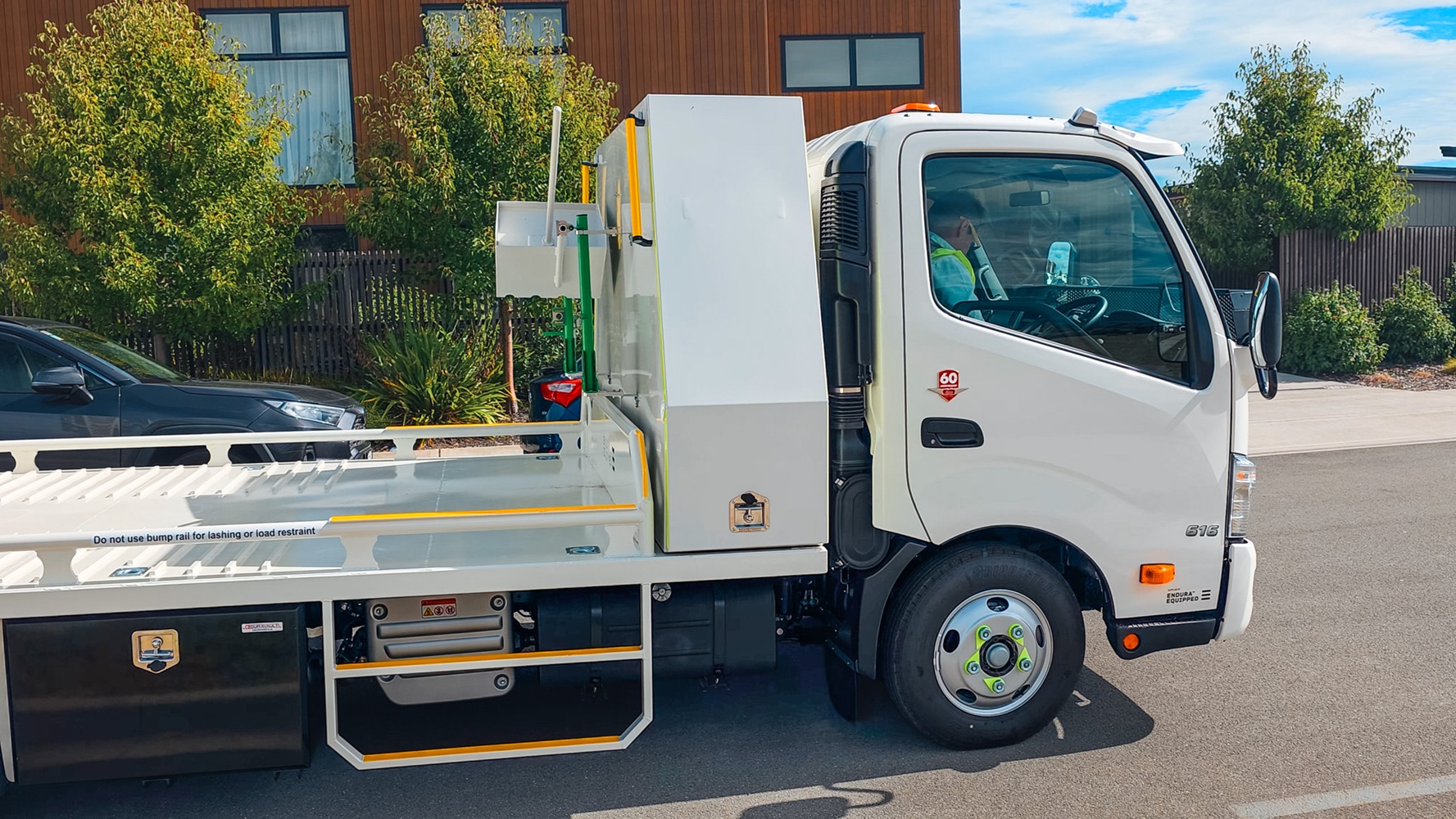 A compact Class 1 transporter truck with a split hydraulic ramp on the back and toolboxes mounted behind the cab.