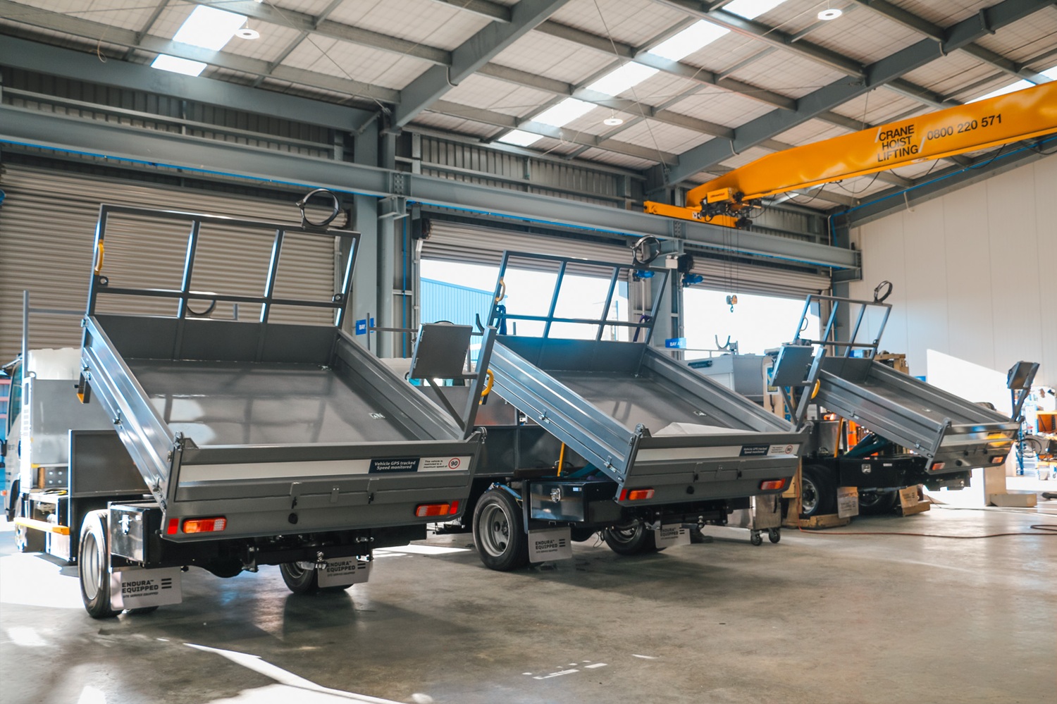 Four identical water utilities trucks lined up in a workshop, almost ready to be delivered to the customer.